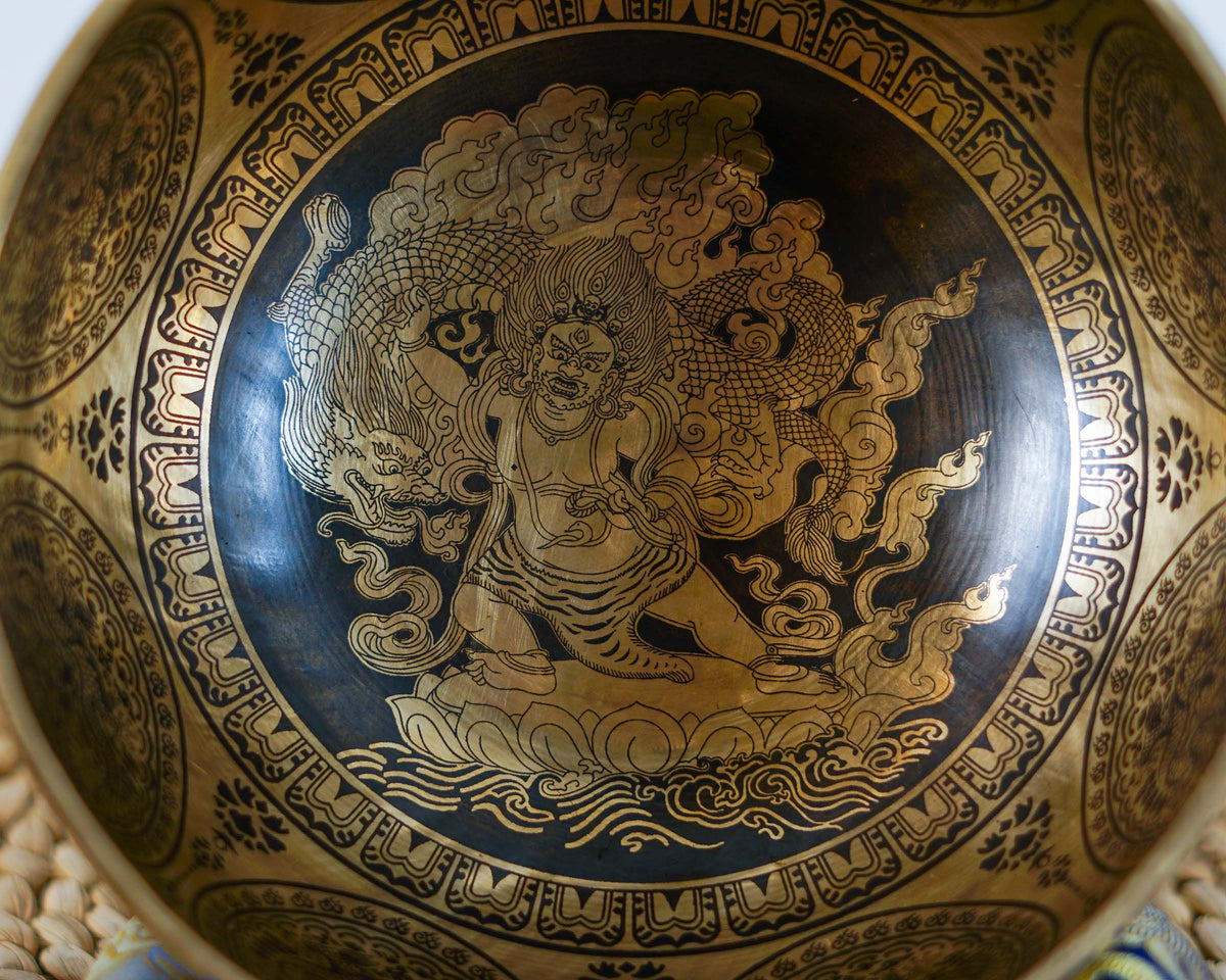 Close up of Mahakala engraved inside a golden singing bowl with intricate flames and traditional Buddhist decorative patterns.