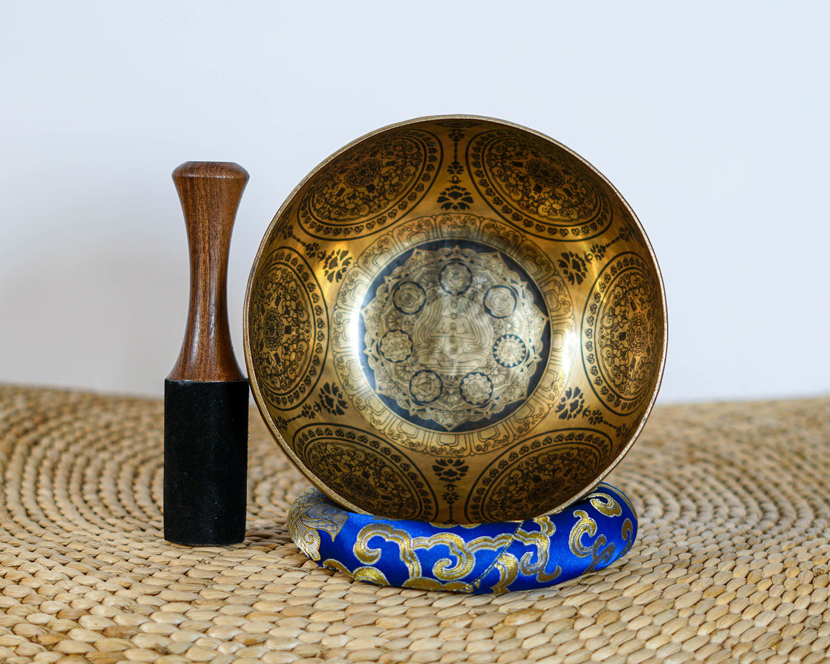 Engraved Seven Chakra Singing Bowl displayed upright with a wooden mallet and blue cushion, showing the central meditation design.