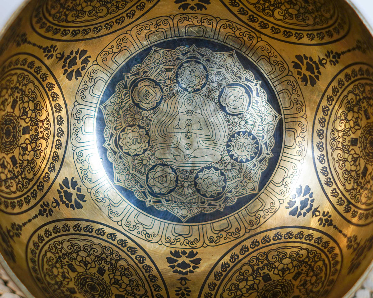 Close up of the seven chakra symbols and meditating figure engraved inside a golden Seven Chakra Singing Bowl.