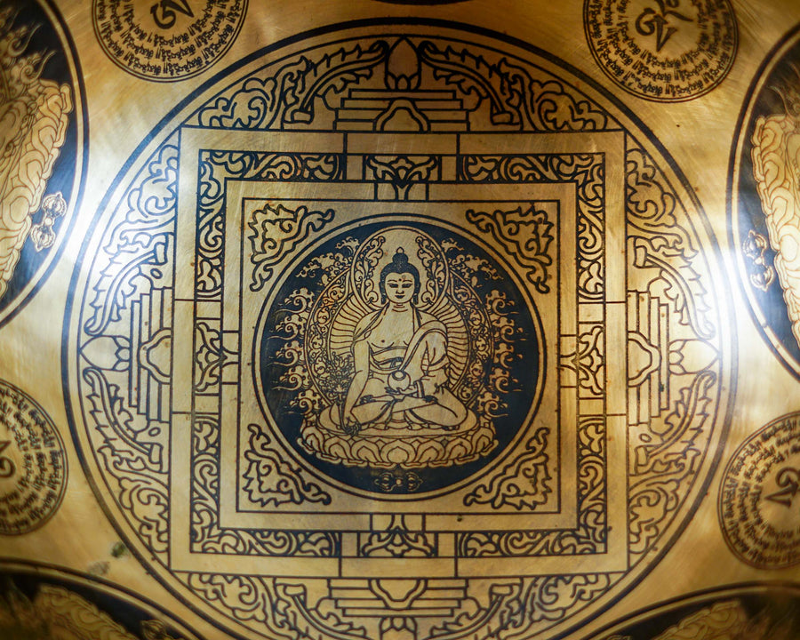 Close up of Buddha seated on a lotus throne inside an engraved geometric mandala on a golden bronze tone singing bowl