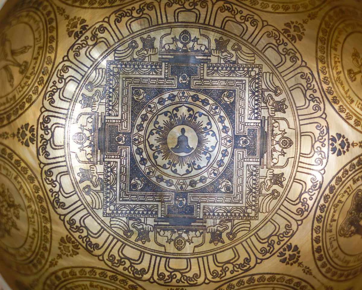 Close up of the engraved Kalchakra inspired mandala and meditating figure inside a golden toned singing bowl.