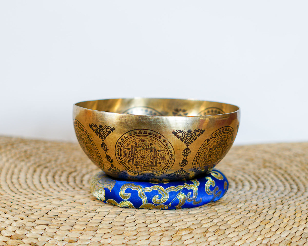 Om Mani Padme Hum Mandala Singing Bowl displayed on a blue brocade cushion, featuring intricate Buddhist decorative engravings.