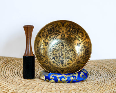 Engraved Om Mani Padme Hum Mandala Singing Bowl displayed upright with a wooden mallet and blue cushion.