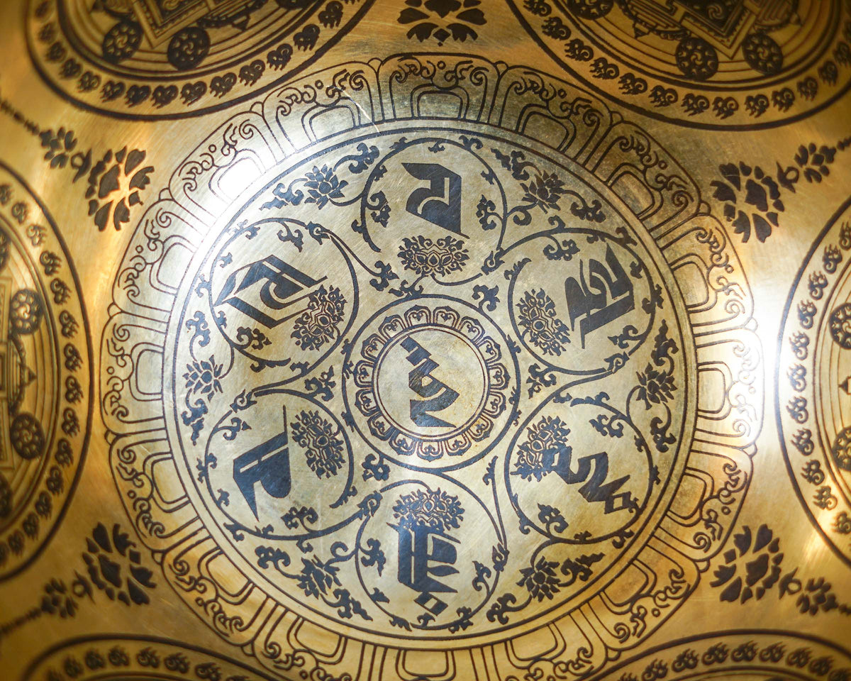 Close up of the Om Mani Padme Hum mantra and circular mandala engraving inside a golden toned singing bowl.