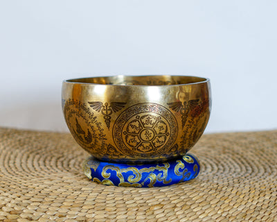 Golden Tree of Life singing bowl featuring intricate Tibetan inspired engravings on the exterior, displayed on a blue brocade cushion