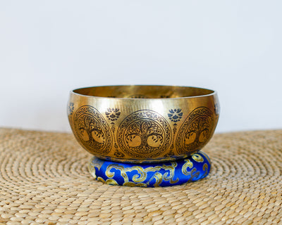 Tree of Life engraved singing bowl displayed on a blue brocade cushion with decorative Himalayan patterns.