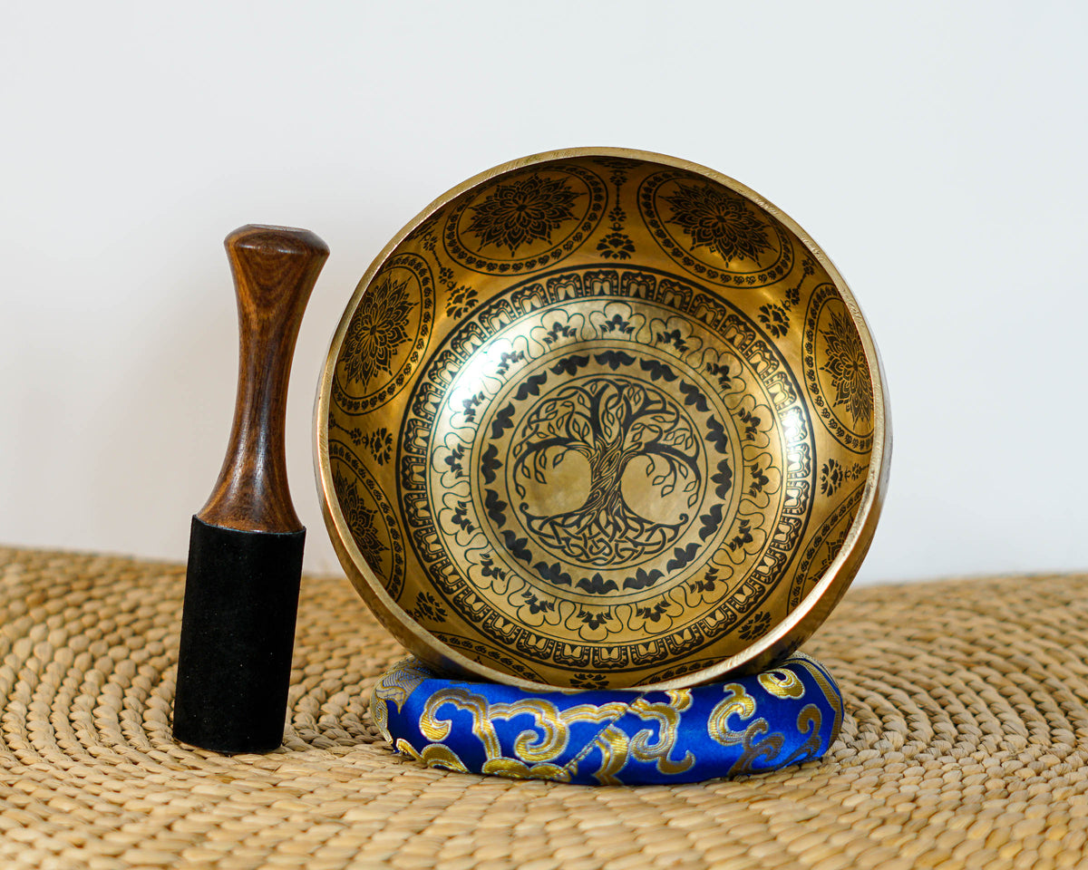 Tree of Life singing bowl shown upright on a blue cushion with a wooden mallet beside it.