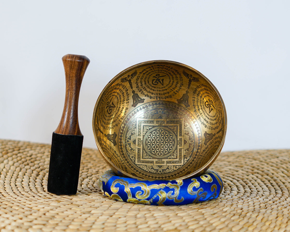 Golden toned Kal Mandala singing bowl with intricate geometric engravings displayed on a blue brocade cushion.