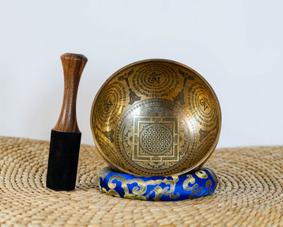 Golden toned Kal Mandala singing bowl with intricate geometric engravings displayed on a blue brocade cushion.
