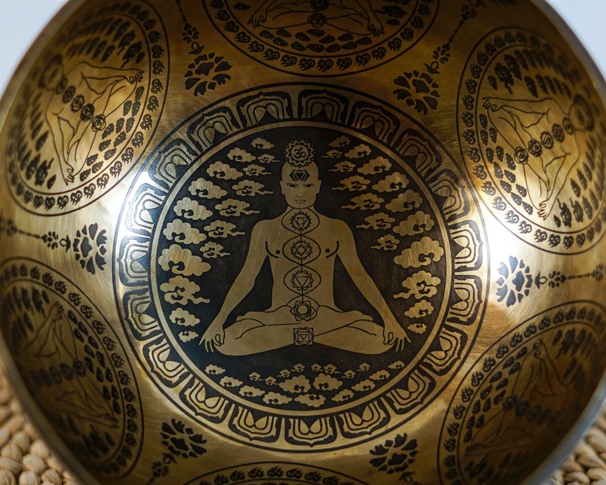 Seven Chakra engraved singing bowl shown upright with a wooden mallet and blue cushion.