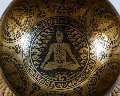 Seven Chakra engraved singing bowl shown upright with a wooden mallet and blue cushion.