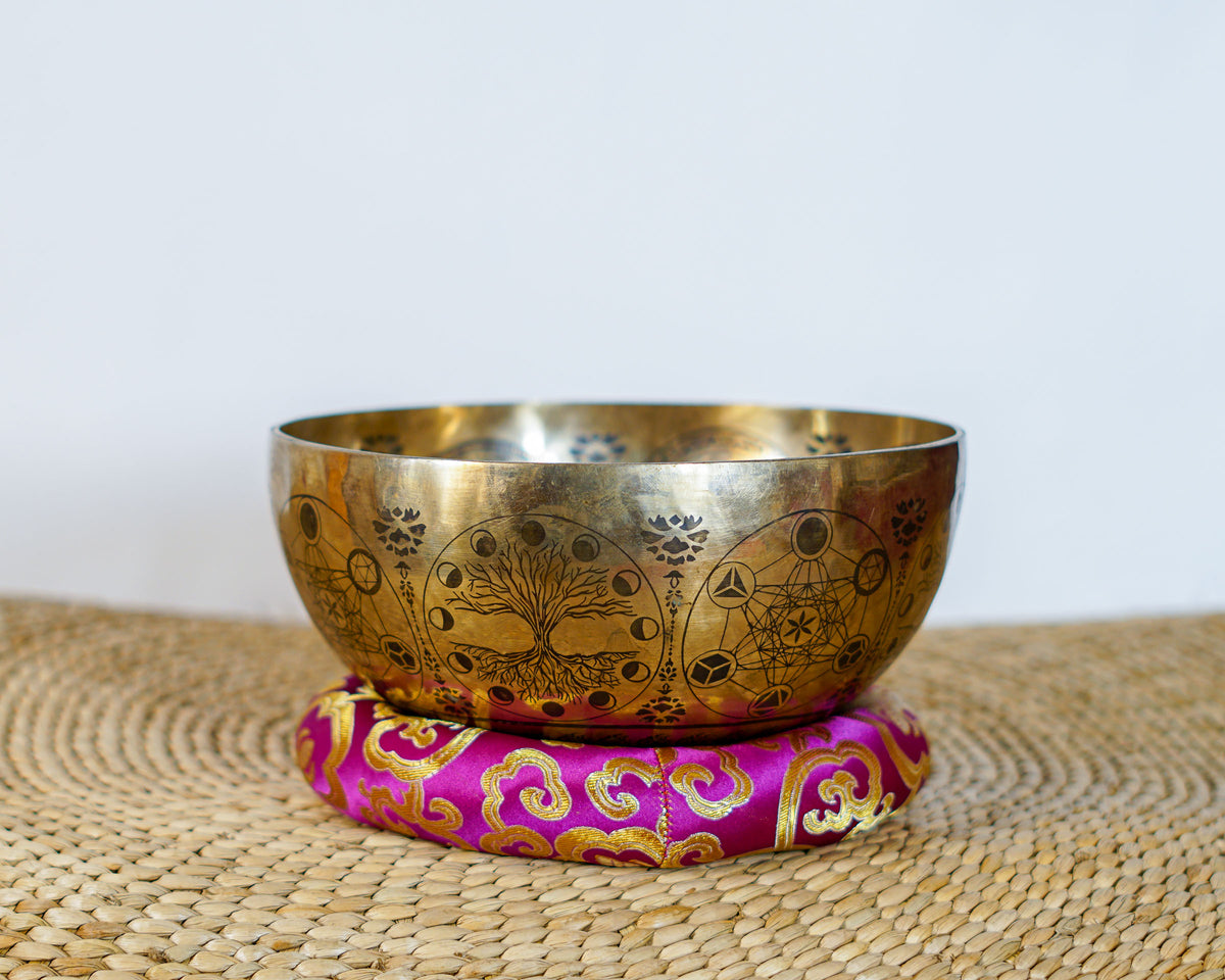 Golden Universe engraved singing bowl displayed on a pink brocade cushion with cosmic decorative patterns.