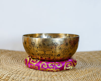Golden Universe engraved singing bowl displayed on a pink brocade cushion with cosmic decorative patterns.