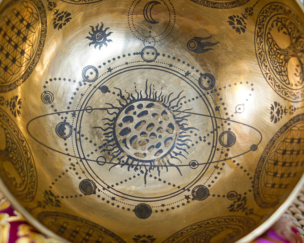 Close up of a Universe singing bowl engraved with a celestial sun, planetary orbits, stars, and moon motifs.
