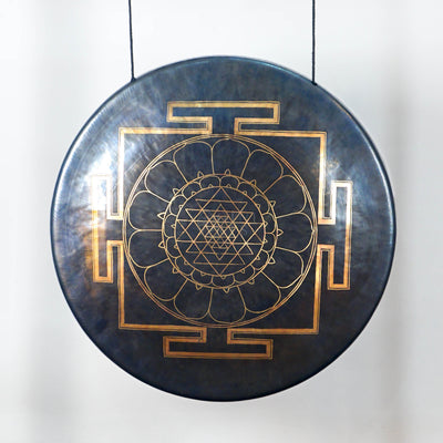 Close-up of a dark metallic gong showing its detailed gold Sri Yantra-inspired geometric mandala and lotus-petal design.