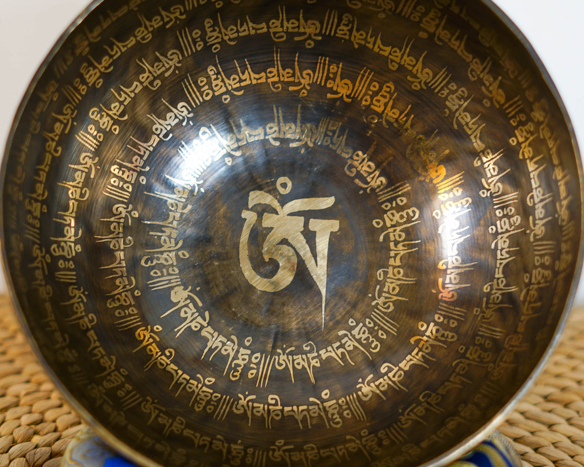Close up of an Om Mantra singing bowl interior featuring a central golden Om symbol surrounded by engraved Tibetan script.