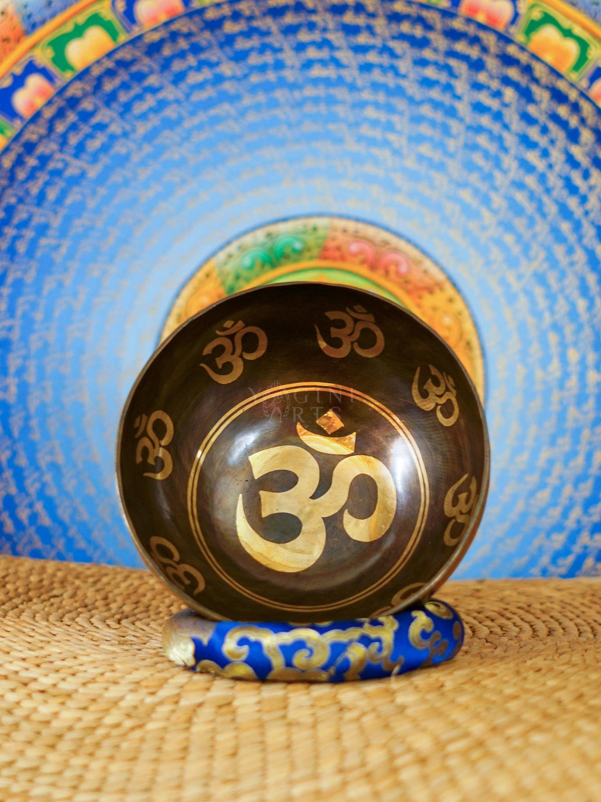 Handcrafted Om singing bowl from Nepal with golden Om engravings, dark bronze finish, decorative blue cushion and wooden striker.