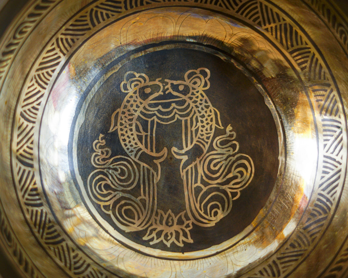Close up of the Two Golden Fish symbol engraved inside a gold and dark bronze singing bowl.