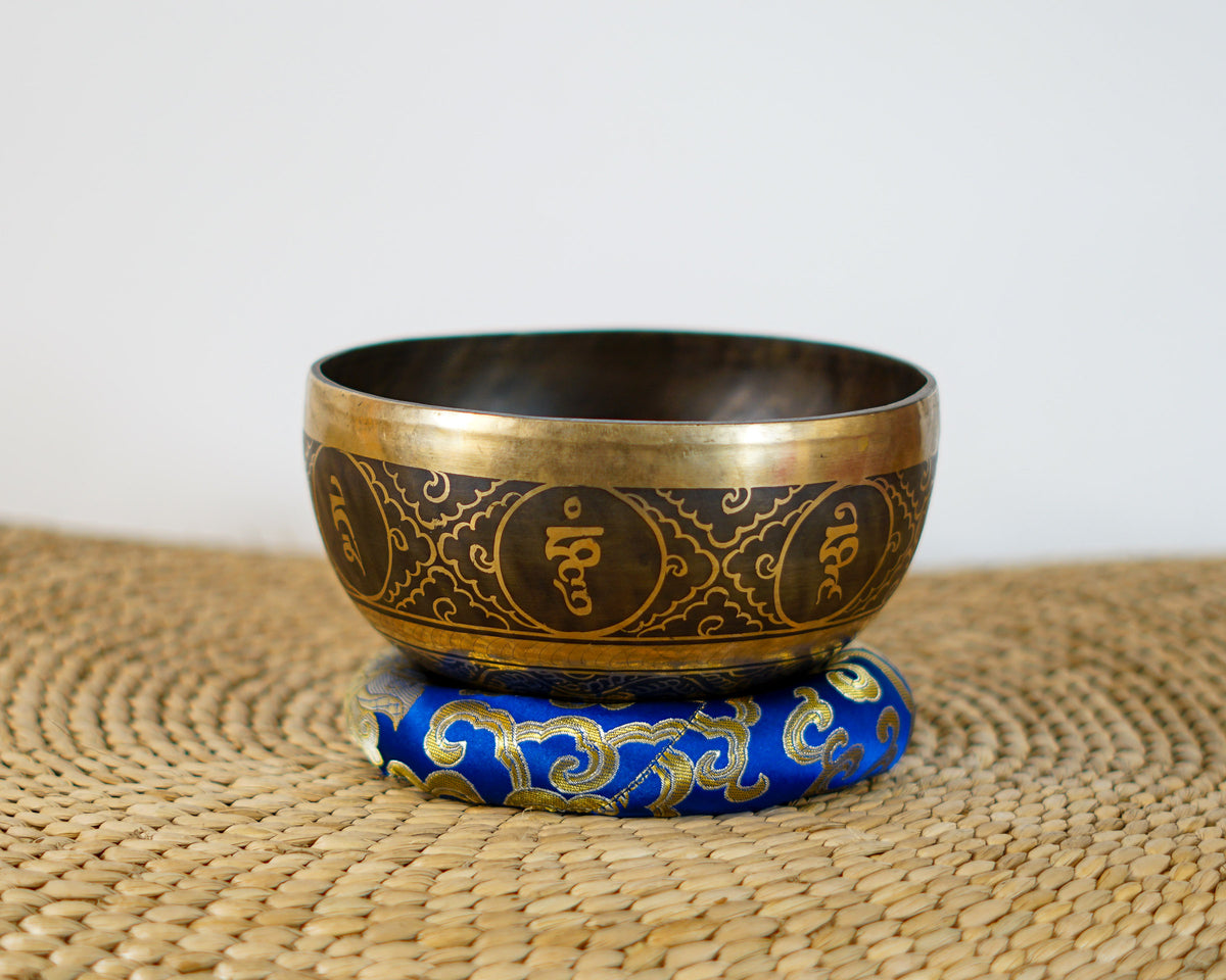 Handmade Himalayan singing bowl featuring a conch shell engraving inside, displayed with a blue brocade cushion and wooden mallet.