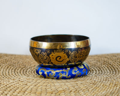 Buddha Eye singing bowl displaying engraved Wisdom Eyes inside the bowl with a wooden mallet and blue brocade cushion.