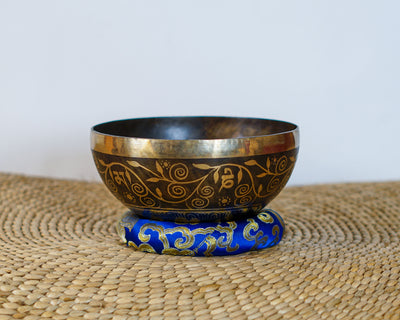 Handmade style Tree of Life singing bowl with golden decorative vine engravings on a blue brocade cushion.