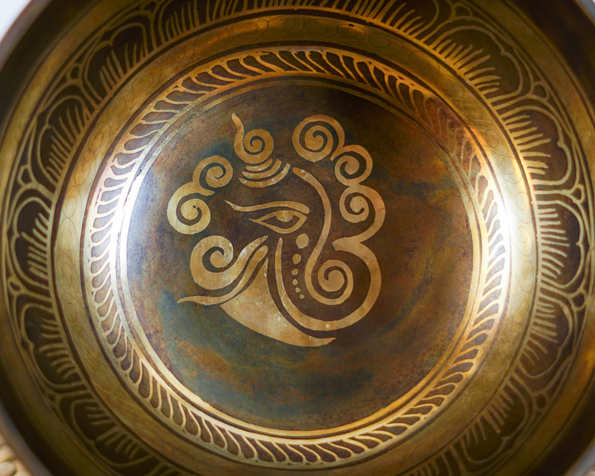 Close up of the golden Ganesh engraving inside a dark antique finish singing bowl with ornate circular borders.