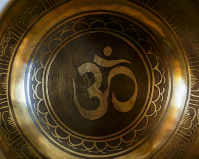 Close up of the sacred Om symbol engraved inside a golden Hindu singing bowl with an antique finish.