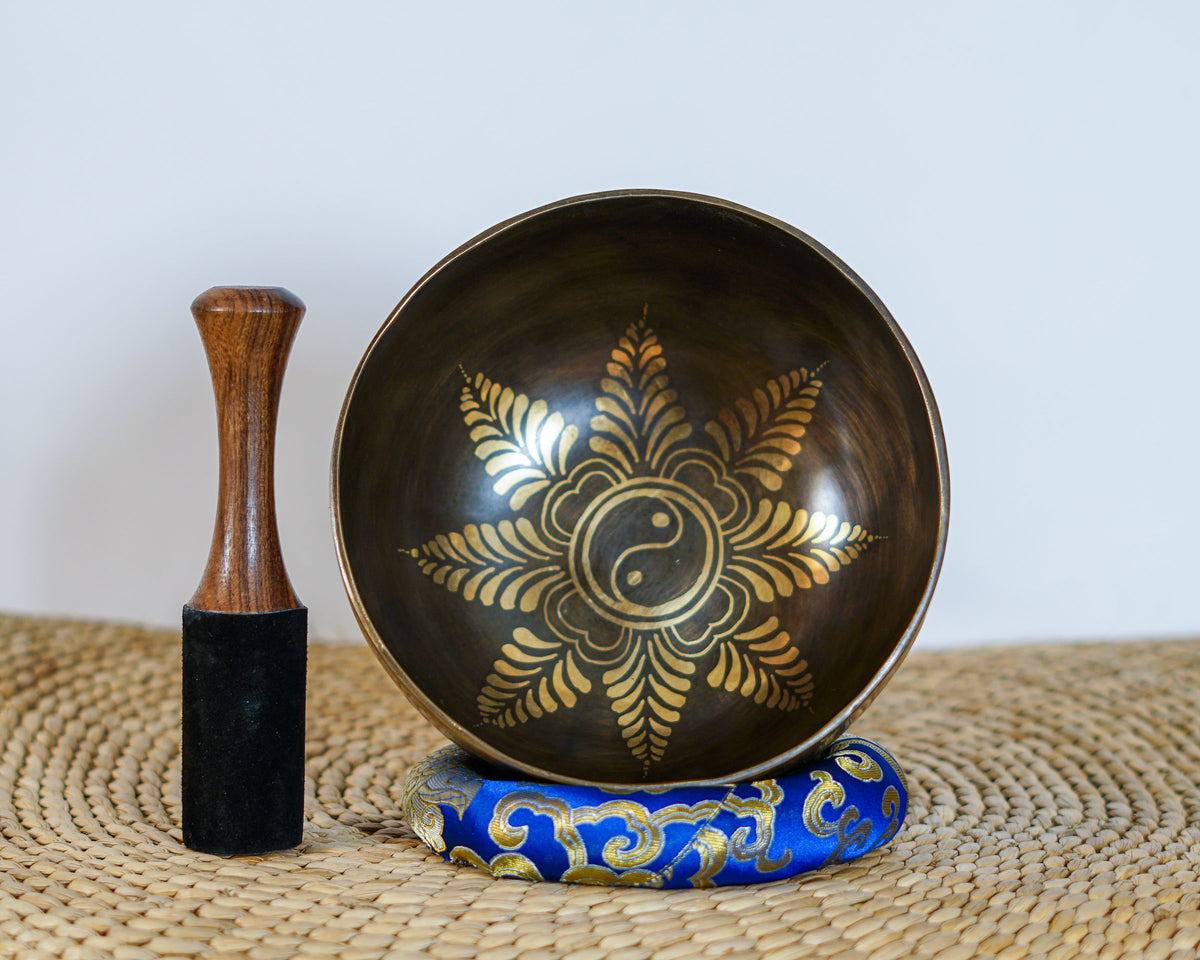 Flower Yin Yang singing bowl displayed upright with a wooden mallet and blue brocade cushion, showing the engraved interior design.