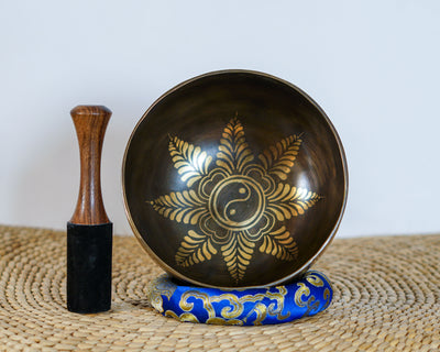 Flower Yin Yang singing bowl displayed upright with a wooden mallet and blue brocade cushion, showing the engraved interior design.