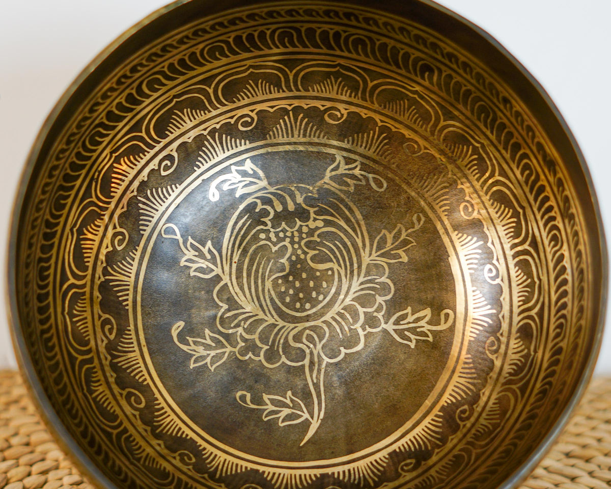 Close up of a golden lotus flower engraving inside a dark antique metal singing bowl with ornate decorative borders.