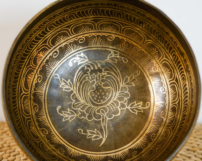 Close up of a golden lotus flower engraving inside a dark antique metal singing bowl with ornate decorative borders.