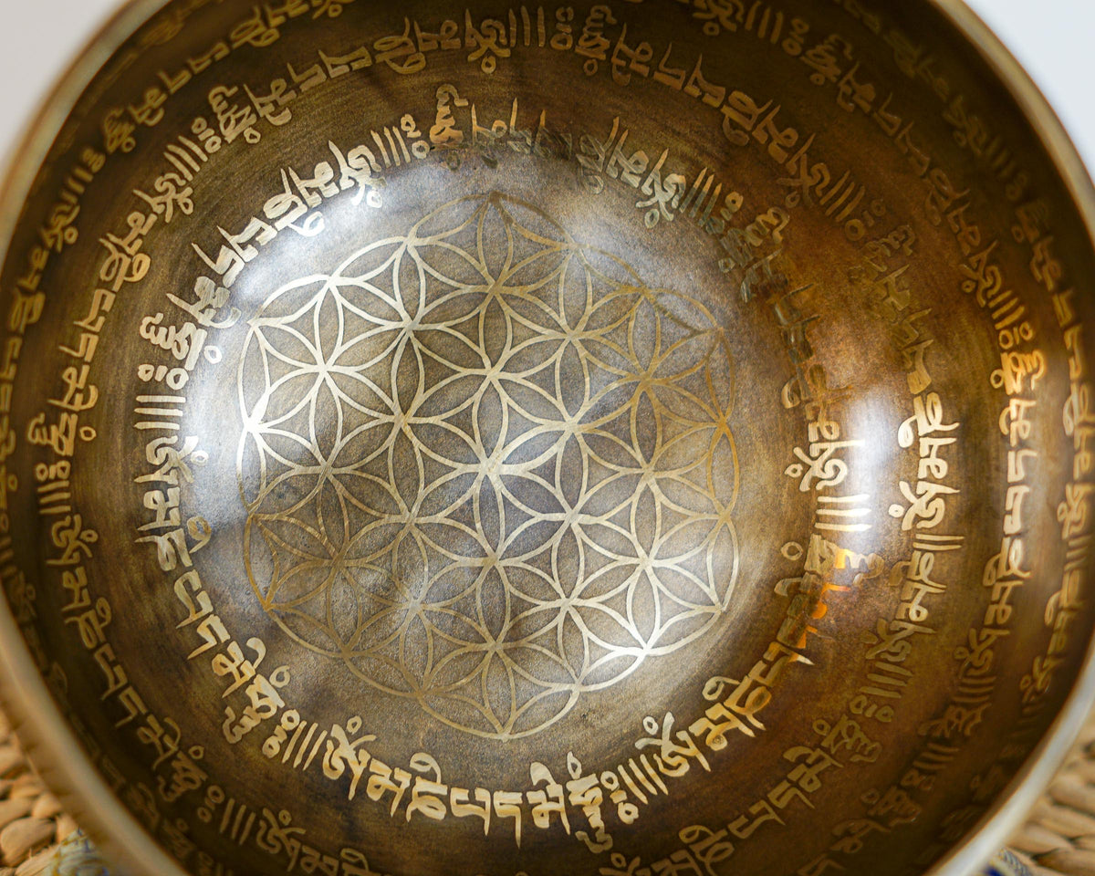 Close up of the Flower of Life geometric engraving surrounded by Tibetan script inside a golden antique finish singing bowl.