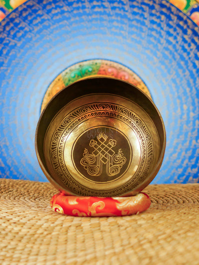 Handcrafted Tibetan singing bowl from Nepal with Buddhist symbol engraving, Tibetan-style script, bronze-gold finish, red cushion and wooden striker.