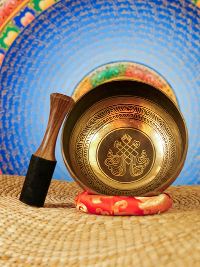 Handcrafted Tibetan singing bowl from Nepal with Buddhist symbol engraving, Tibetan-style script, bronze-gold finish, red cushion and wooden striker.