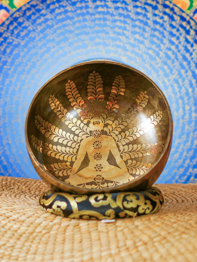 Handcrafted Nepal singing bowl with meditating figure and chakra engraving, floral design, bronze finish, cushion and wooden striker.