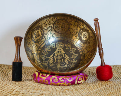 Chakra Manab engraved singing bowl shown upright with a meditating figure design, decorative borders, brocade cushion, and wooden strikers.