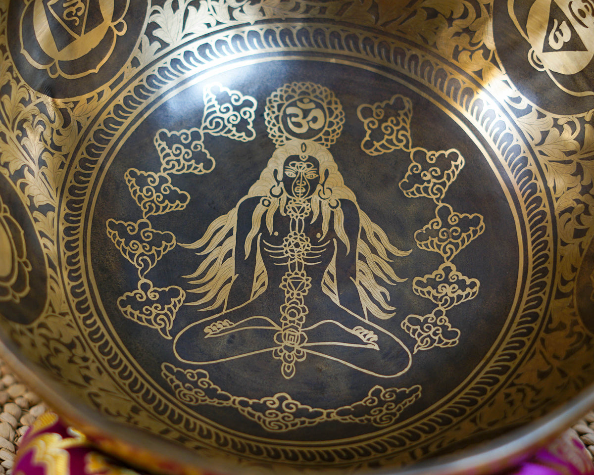 Close up of the Chakra Manab singing bowl interior showing an engraved meditating figure, chakra symbols, Om motif, and decorative cloud patterns.