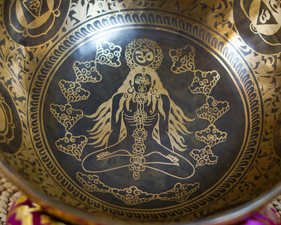 Close up of the Chakra Manab singing bowl interior showing an engraved meditating figure, chakra symbols, Om motif, and decorative cloud patterns.
