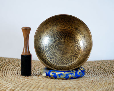 Dove engraved Tibetan singing bowl displayed upright with intricate geometric patterns, a blue brocade cushion, and a wooden striker.