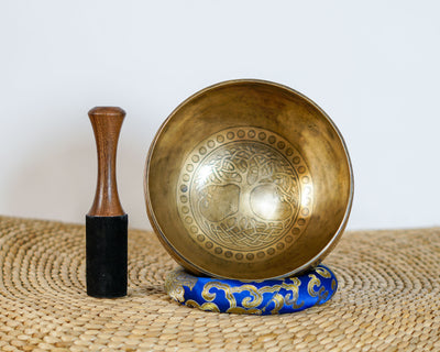 Tree of Life engraved Tibetan singing bowl displayed upright with a wooden striker and blue brocade cushion, showing the detailed interior artwork.