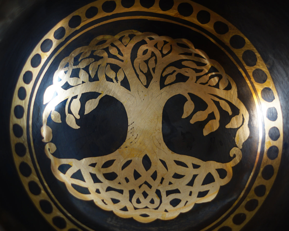 Close up of a golden Tree of Life engraving inside a dark bronze Tibetan singing bowl, showing detailed branches, roots, and a circular dotted border.