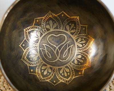 Close up of a golden Swan Symbol of Life motif with a heart and lotus inspired mandala engraved inside a dark antique Tibetan singing bowl.