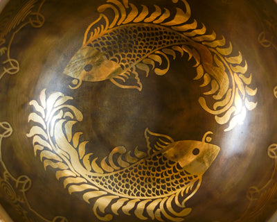 Close up of the golden twin fish pair intricately engraved inside a dark antique bronze Tibetan singing bowl.