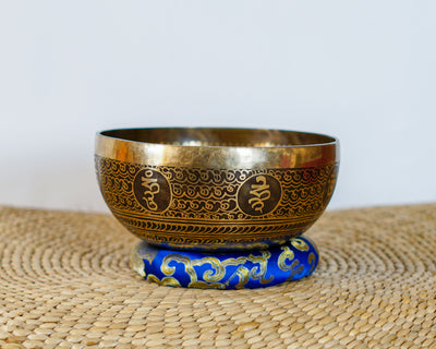 Golden Flower of Life Tibetan singing bowl with decorative Tibetan script displayed on a blue brocade cushion.