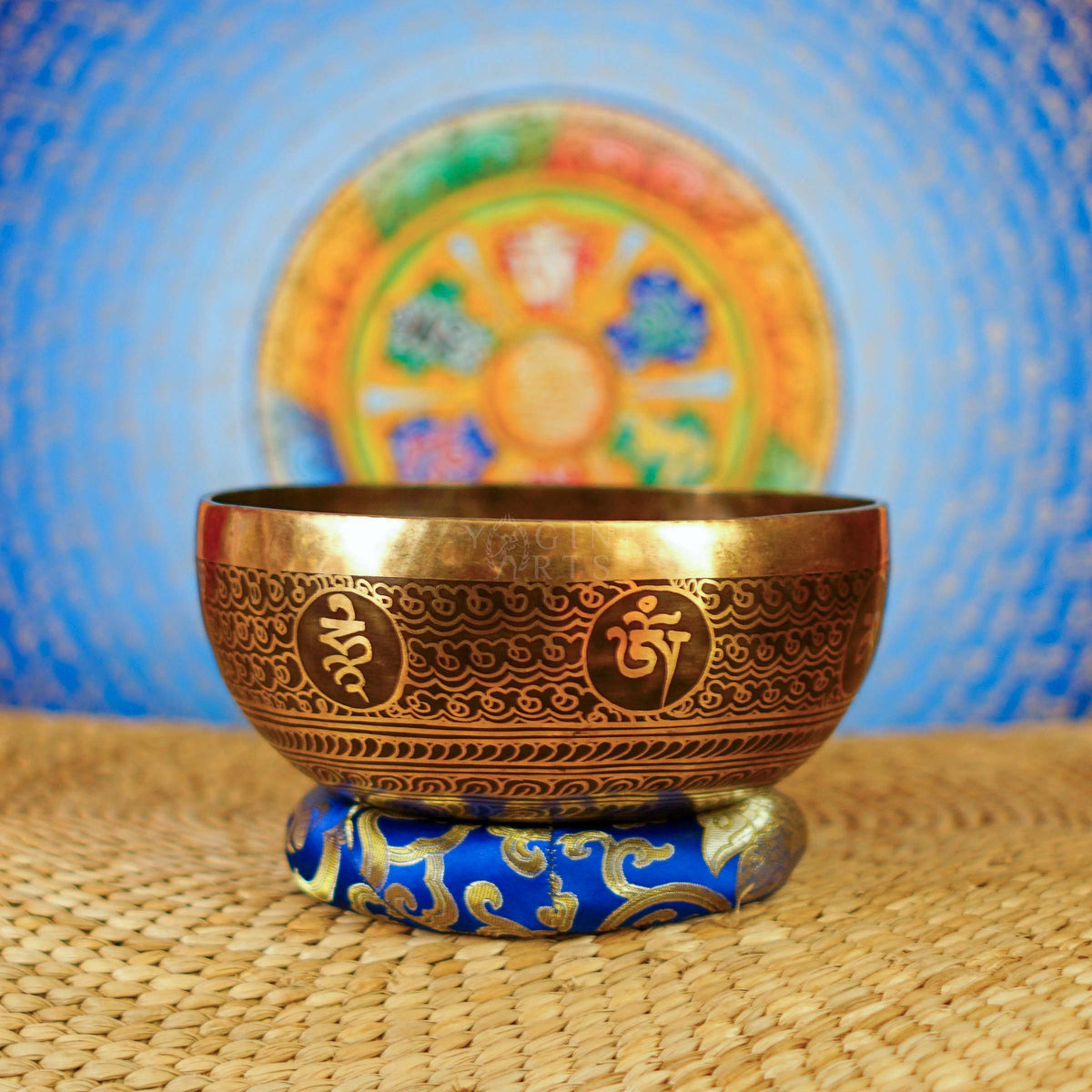 Handcrafted Flower of Life singing bowl from Nepal with sacred geometry engraving, Tibetan-style motifs, bronze-gold finish and blue cushion.
