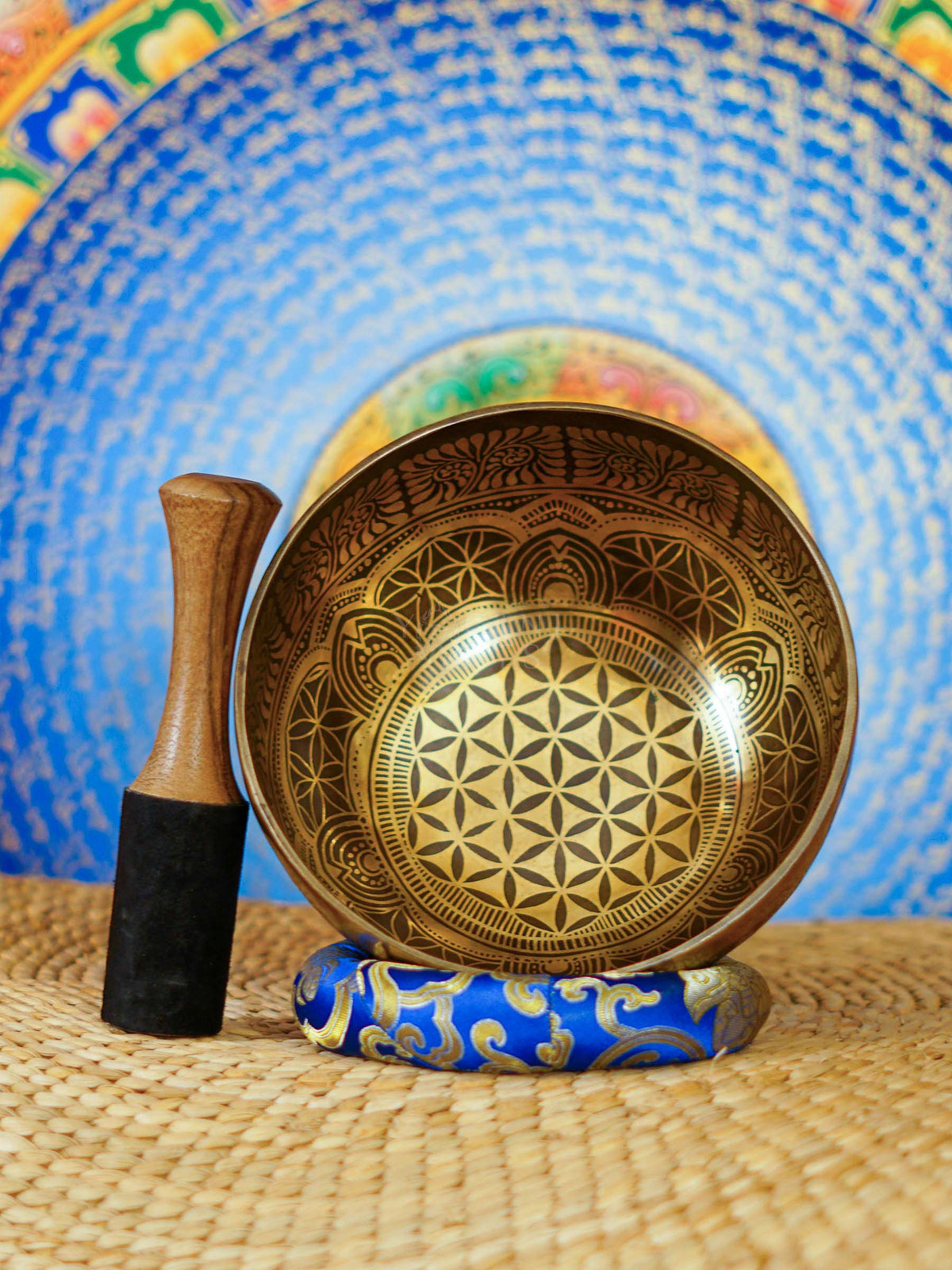 Handcrafted Flower of Life singing bowl from Nepal with sacred geometry engraving, Tibetan-style motifs, bronze-gold finish and blue cushion.
