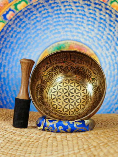 Handcrafted Flower of Life singing bowl from Nepal with sacred geometry engraving, Tibetan-style motifs, bronze-gold finish and blue cushion.