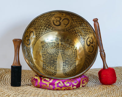 Buddha footprint singing bowl shown upright with wooden mallets and a pink brocade cushion, highlighting the traditional engraved design.
