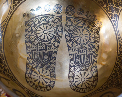 Close up of sacred Buddha footprints engraved inside a golden Tibetan singing bowl with intricate floral details.