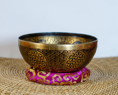 Golden Chengresi Tibetan singing bowl featuring sacred Buddhist engravings and geometric floral designs on a pink brocade cushion.